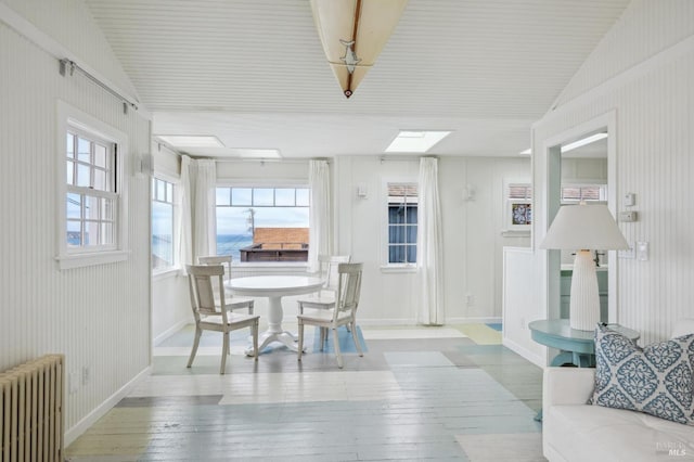 dining space featuring lofted ceiling with skylight, radiator, and light wood-type flooring