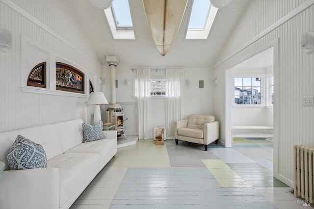 living room featuring radiator heating unit, lofted ceiling with skylight, a wood stove, and a wealth of natural light