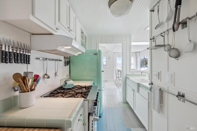 kitchen with white cabinetry, stainless steel gas range, and tile countertops