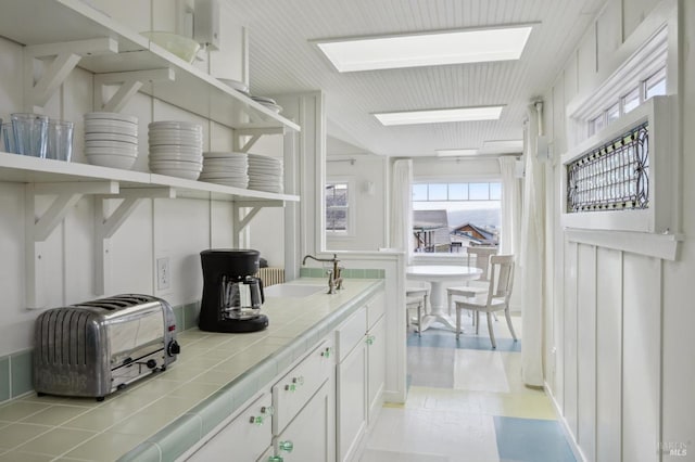 interior space featuring sink, a skylight, tile counters, and white cabinets