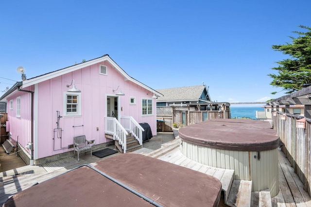 rear view of house with a deck with water view and a covered hot tub