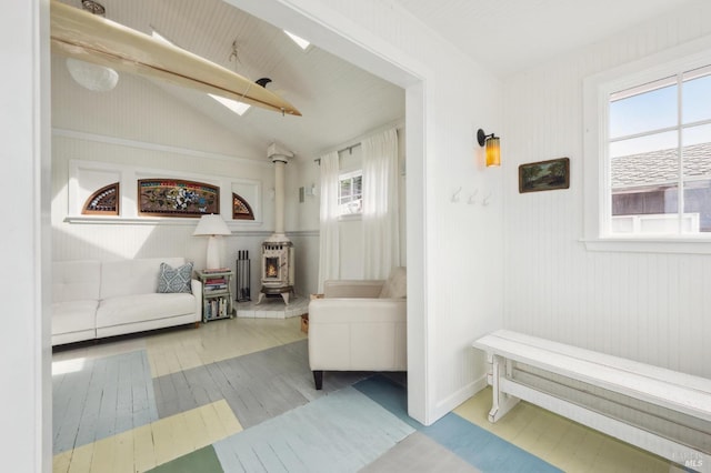 sitting room with lofted ceiling with skylight, a wealth of natural light, light wood-type flooring, and a wood stove