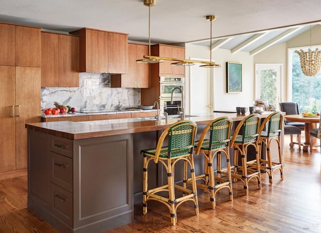 kitchen featuring lofted ceiling with beams, stainless steel double oven, brown cabinets, tasteful backsplash, and pendant lighting