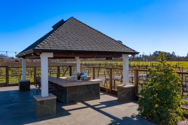 view of patio with a bar, an outdoor kitchen, a grill, a gazebo, and a rural view