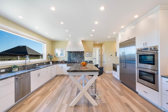 kitchen featuring appliances with stainless steel finishes, sink, white cabinets, custom exhaust hood, and light wood-type flooring