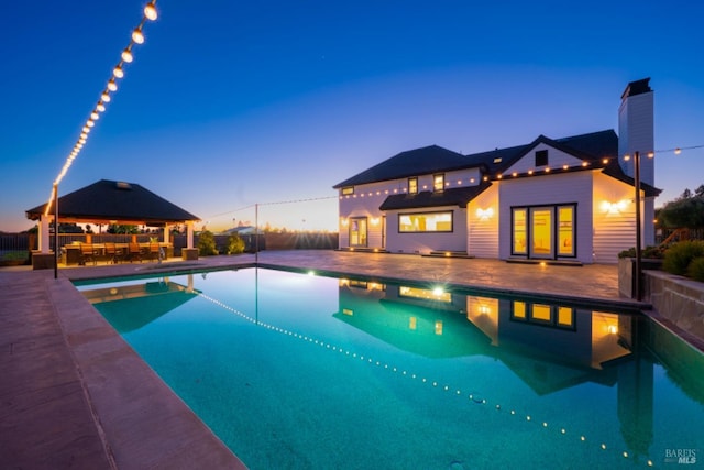 pool at dusk featuring a gazebo and a patio