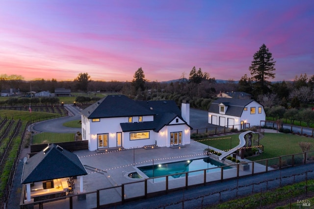 back house at dusk with a fenced in pool, a patio, and a lawn