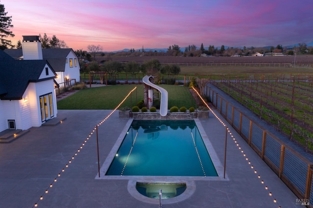 pool at dusk with a rural view, a yard, a patio, and a water slide