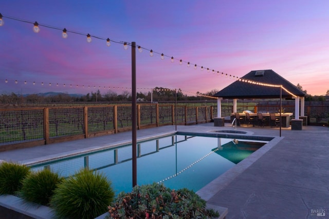 pool at dusk with an in ground hot tub, a gazebo, and a patio area