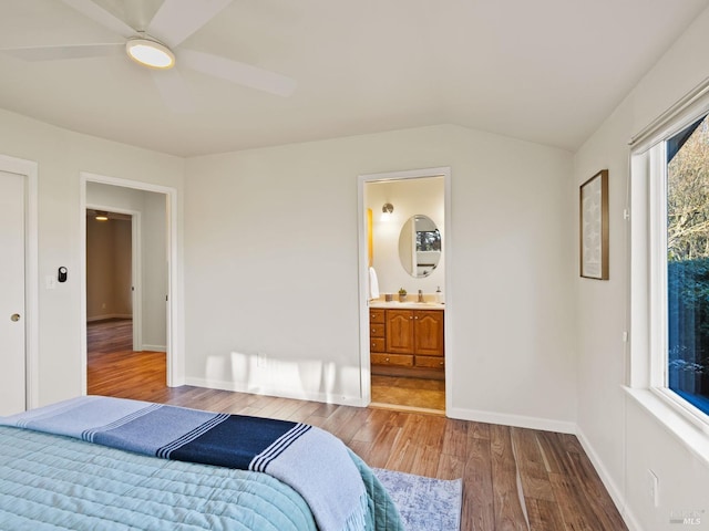 bedroom featuring baseboards, wood finished floors, ensuite bathroom, vaulted ceiling, and a sink