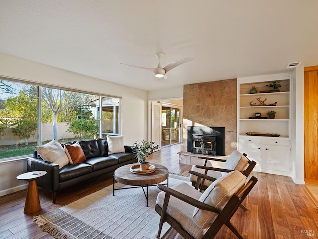 living room featuring built in features, baseboards, visible vents, light wood-style floors, and ceiling fan