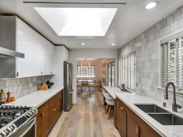 kitchen with wall chimney exhaust hood, sink, white cabinetry, hanging light fixtures, and stainless steel fridge