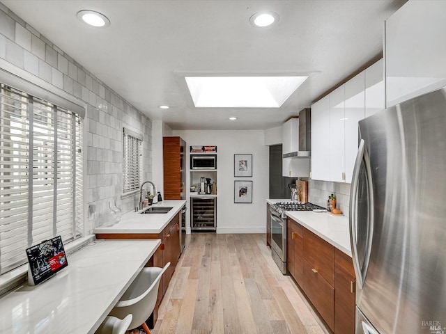 kitchen featuring wall chimney range hood, sink, a skylight, stainless steel appliances, and beverage cooler