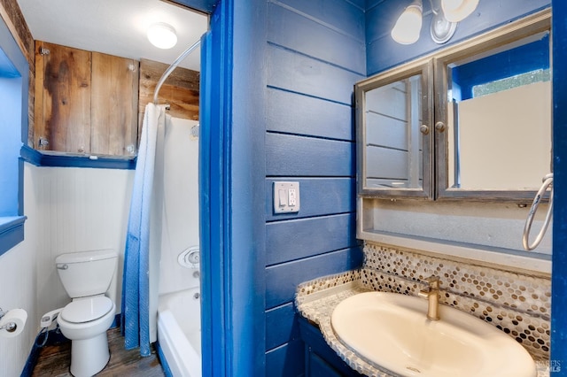 full bathroom with sink, shower / bathtub combination with curtain, wooden walls, and toilet