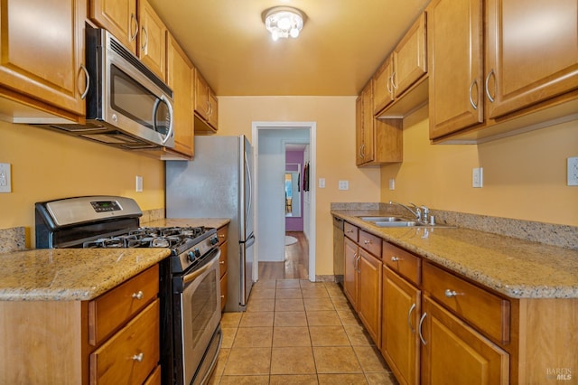 kitchen with stainless steel appliances, light tile patterned flooring, light stone countertops, and sink