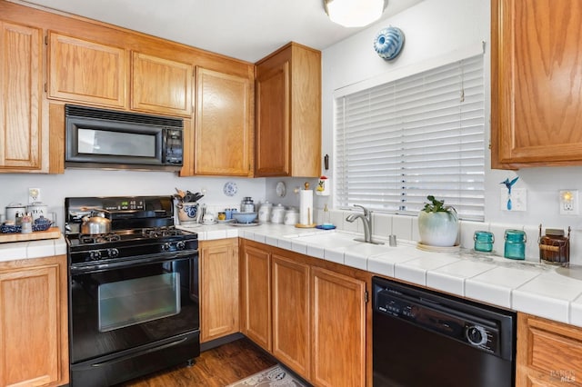 kitchen featuring dark hardwood / wood-style flooring, sink, tile countertops, and black appliances