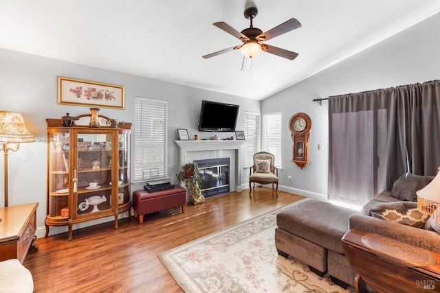 living room featuring wood-type flooring, a tile fireplace, ceiling fan, and vaulted ceiling