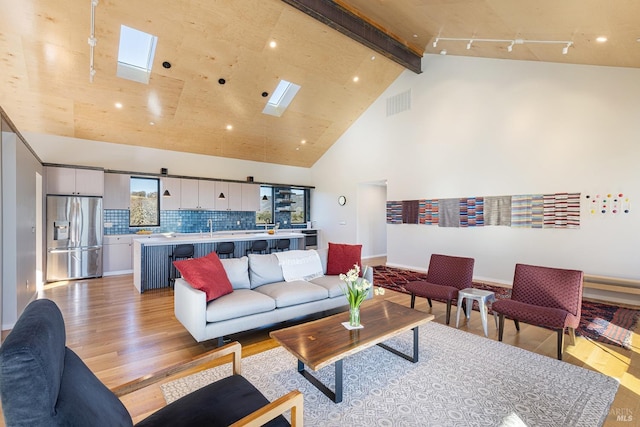 living room with sink, a skylight, high vaulted ceiling, light wood-type flooring, and beam ceiling