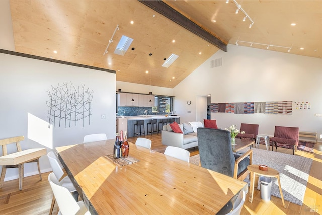 dining area featuring rail lighting, beam ceiling, a skylight, high vaulted ceiling, and light hardwood / wood-style floors