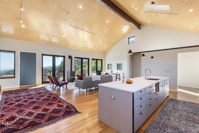 kitchen with sink, high vaulted ceiling, light wood-type flooring, gray cabinets, and a kitchen island with sink