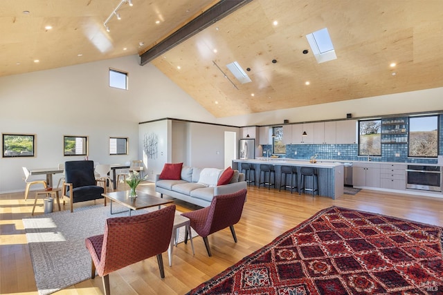 living room with light hardwood / wood-style flooring, beam ceiling, a skylight, and high vaulted ceiling