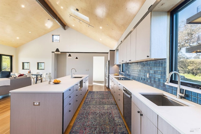 kitchen featuring sink, backsplash, lofted ceiling with skylight, and a center island with sink