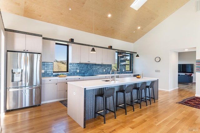 kitchen with high vaulted ceiling, an island with sink, a breakfast bar, and stainless steel fridge with ice dispenser