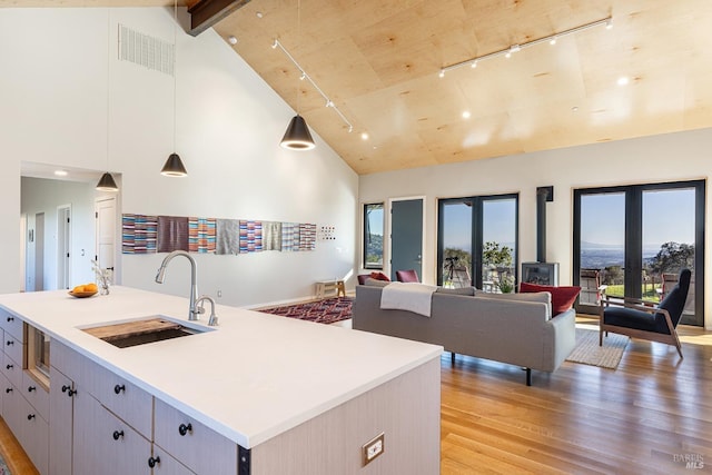 kitchen with sink, high vaulted ceiling, a center island with sink, pendant lighting, and beam ceiling