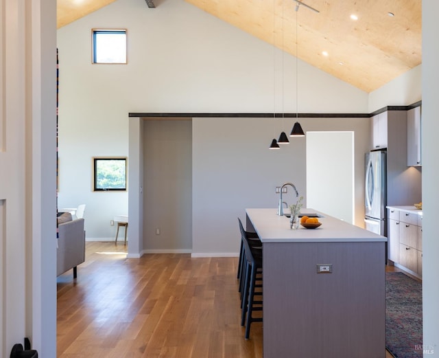 kitchen with sink, hardwood / wood-style flooring, stainless steel fridge, hanging light fixtures, and an island with sink