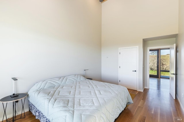 bedroom featuring access to outside, hardwood / wood-style floors, and a towering ceiling