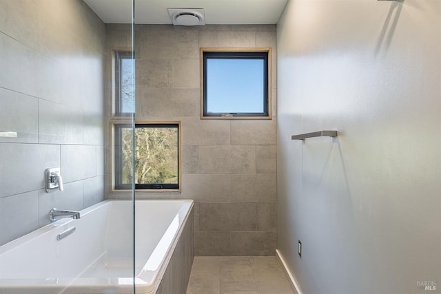 bathroom with a relaxing tiled tub, tile patterned floors, and tile walls