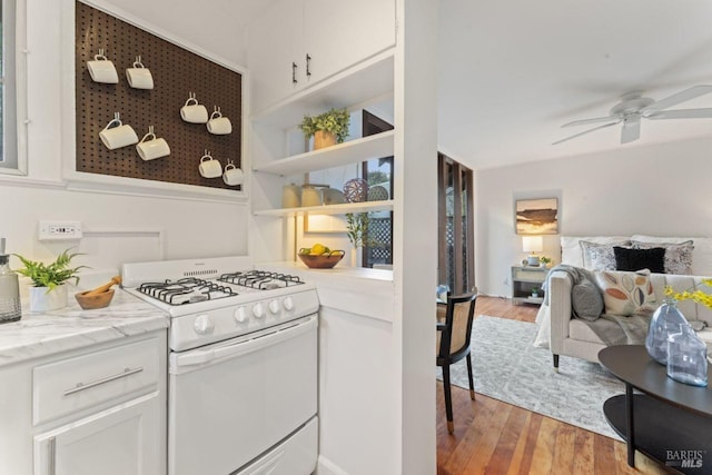 kitchen with white gas range, light stone countertops, light hardwood / wood-style flooring, and white cabinets