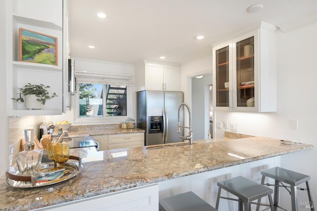 kitchen with white cabinetry, stainless steel fridge, backsplash, kitchen peninsula, and light stone countertops