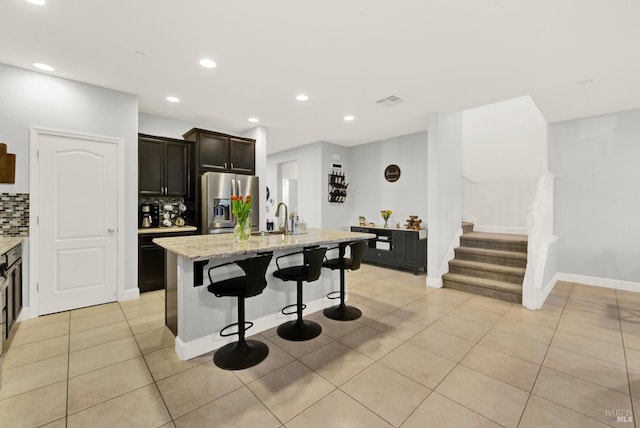 kitchen with light tile patterned floors, stainless steel fridge with ice dispenser, a sink, decorative backsplash, and a kitchen breakfast bar