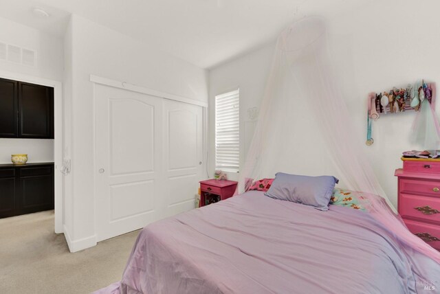 bedroom with a closet, visible vents, and light colored carpet