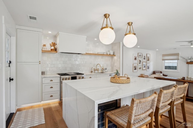 kitchen with sink, light hardwood / wood-style flooring, hanging light fixtures, light stone countertops, and white cabinets