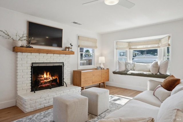 living room with ceiling fan, a fireplace, plenty of natural light, and light wood-type flooring