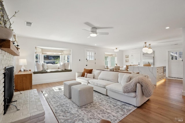 living room featuring ceiling fan, a fireplace, and light wood-type flooring