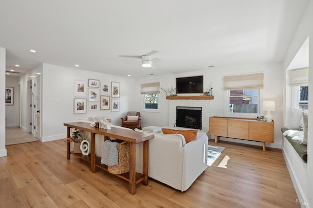 living room featuring ceiling fan, a fireplace, and light wood-type flooring