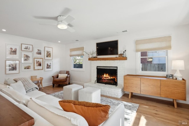 living room featuring ceiling fan, a brick fireplace, and light wood-type flooring