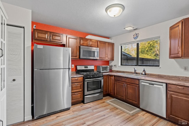 kitchen featuring stainless steel appliances, sink, a textured ceiling, and light hardwood / wood-style flooring