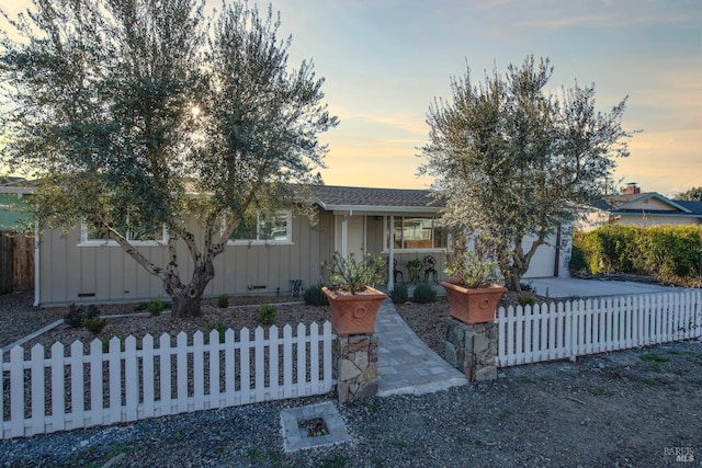 view of front facade with concrete driveway, a fenced front yard, an attached garage, covered porch, and board and batten siding