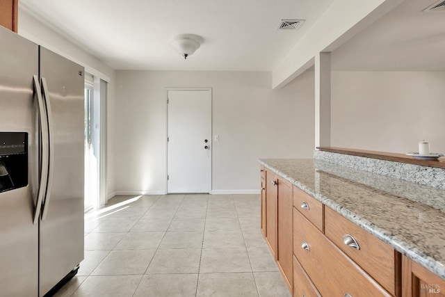 kitchen with stainless steel refrigerator with ice dispenser, light tile patterned floors, visible vents, brown cabinetry, and light stone countertops