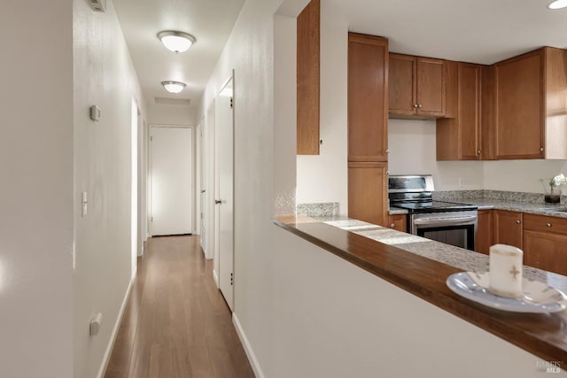 kitchen featuring baseboards, light wood-style floors, light countertops, stainless steel electric stove, and brown cabinetry