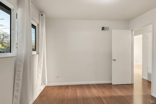 empty room featuring baseboards, plenty of natural light, visible vents, and wood finished floors