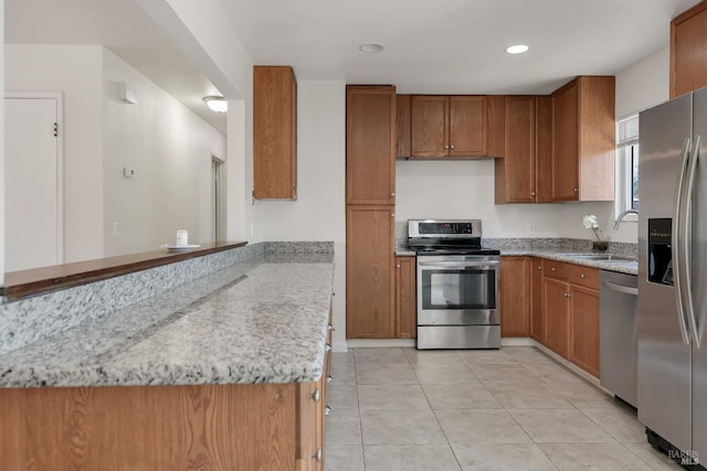 kitchen featuring brown cabinets, light stone countertops, stainless steel appliances, and a sink