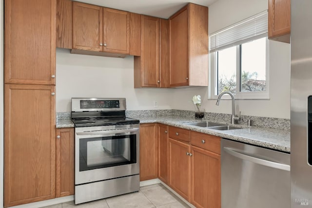 kitchen featuring light tile patterned floors, light stone counters, a sink, appliances with stainless steel finishes, and brown cabinets