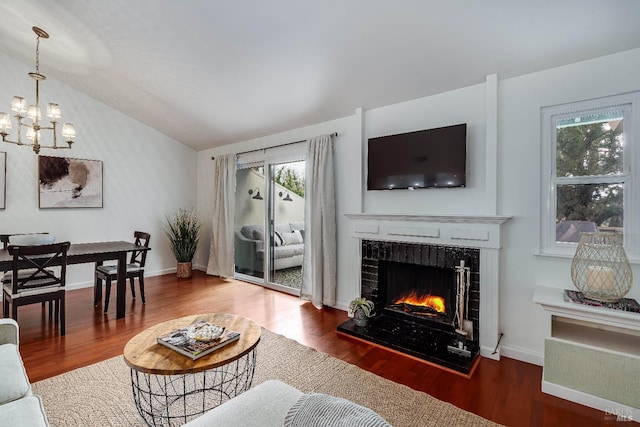 living room with hardwood / wood-style flooring, an inviting chandelier, a tiled fireplace, and vaulted ceiling