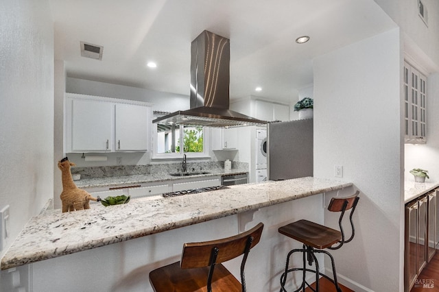 kitchen featuring sink, island range hood, white cabinets, and stacked washing maching and dryer