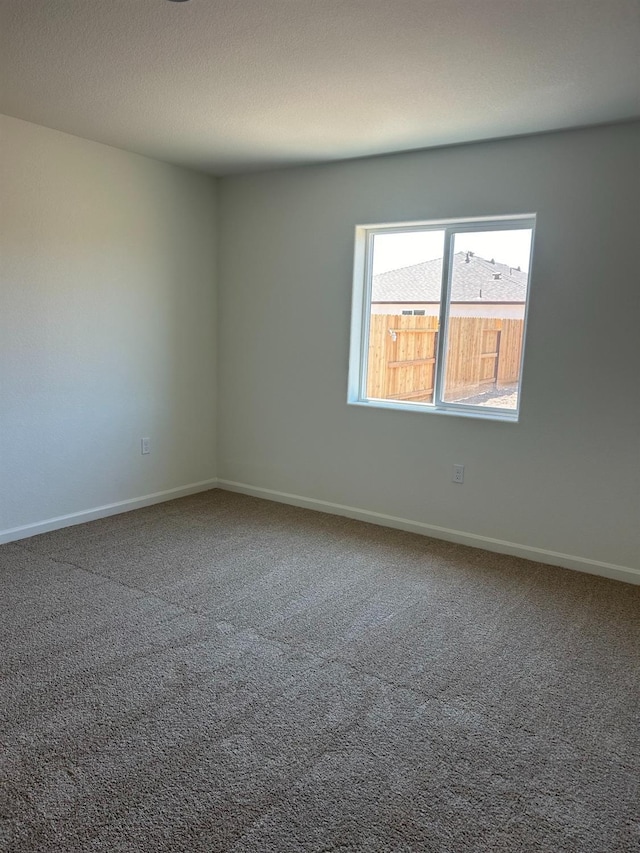 carpeted spare room featuring a textured ceiling and baseboards